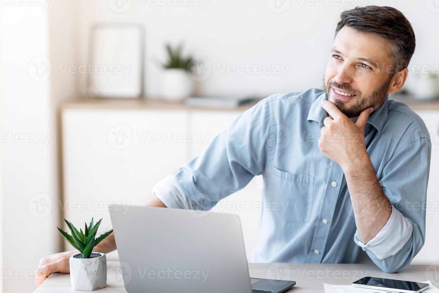 Pensive male entrepreneur thinking about something while working at desk in office, found business solution, looking away with pleased face expression photo
