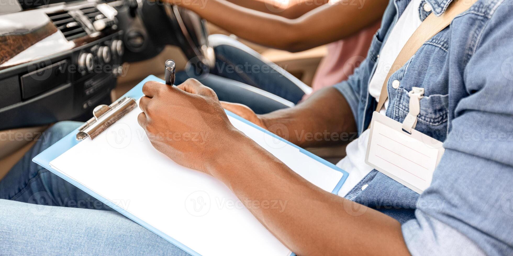 Unrecognizable black man driving instructor taking notes at chart during exam, closeup. Cropped of african american woman attending driving school, passing test, cropped, side view photo