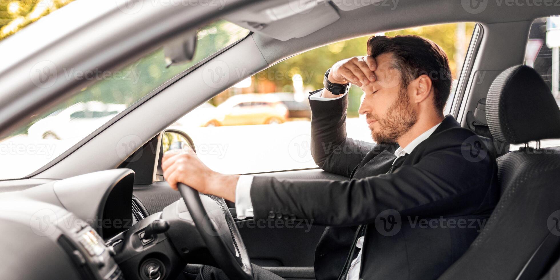 Stressed businessman driving luxury car, stuck in traffic, late to airport, side view, copy space. Frustrated middle-aged man in expensive suit touching his forehead while driving auto photo