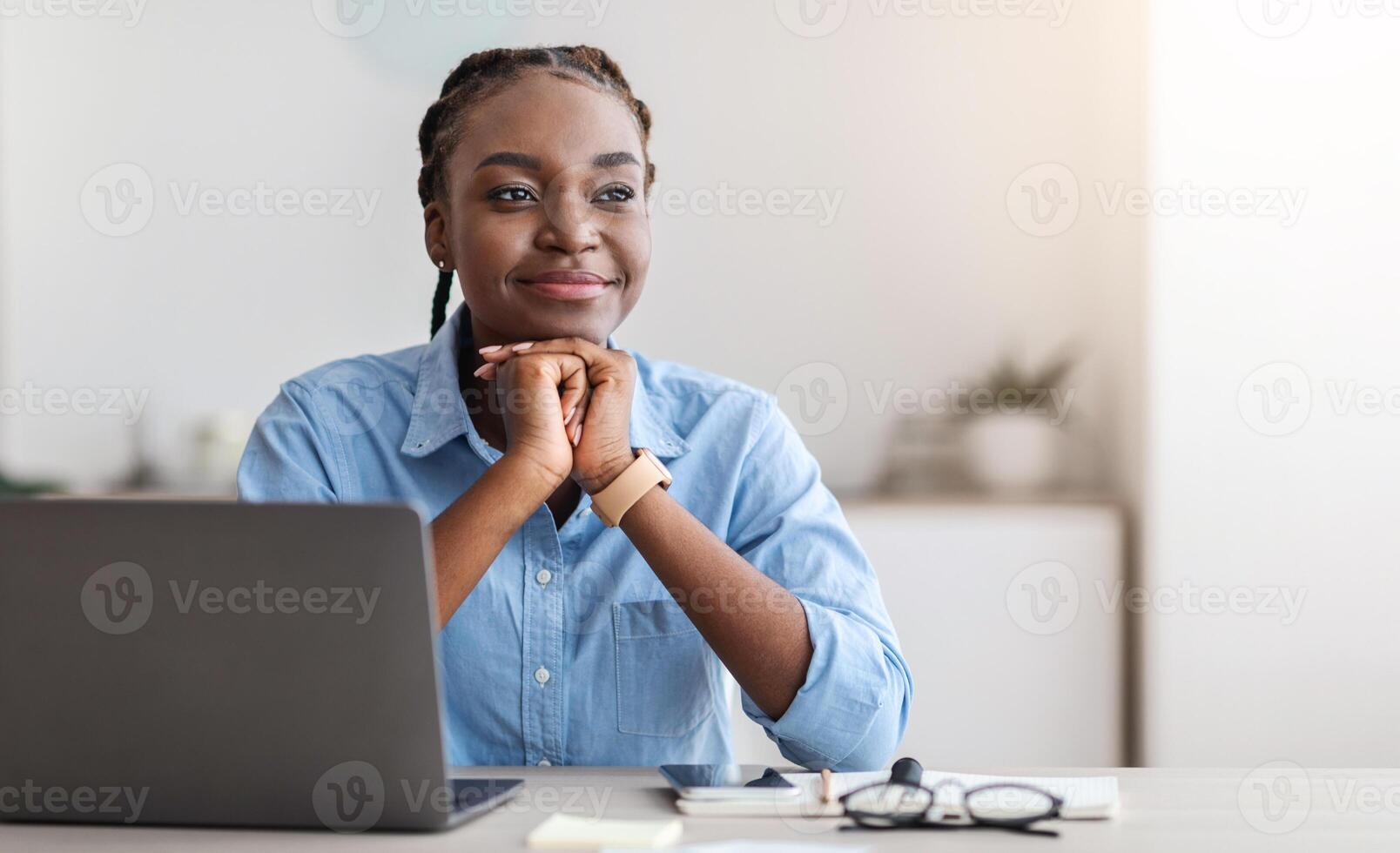 Beautiful Young Black Businesswoman Daydreaming At Workplace In Office, Sitting At Desk With Thoughtful Face Expression, Thinking About Business Plans, Resting Head On Hands And Smiling, Copy Space photo