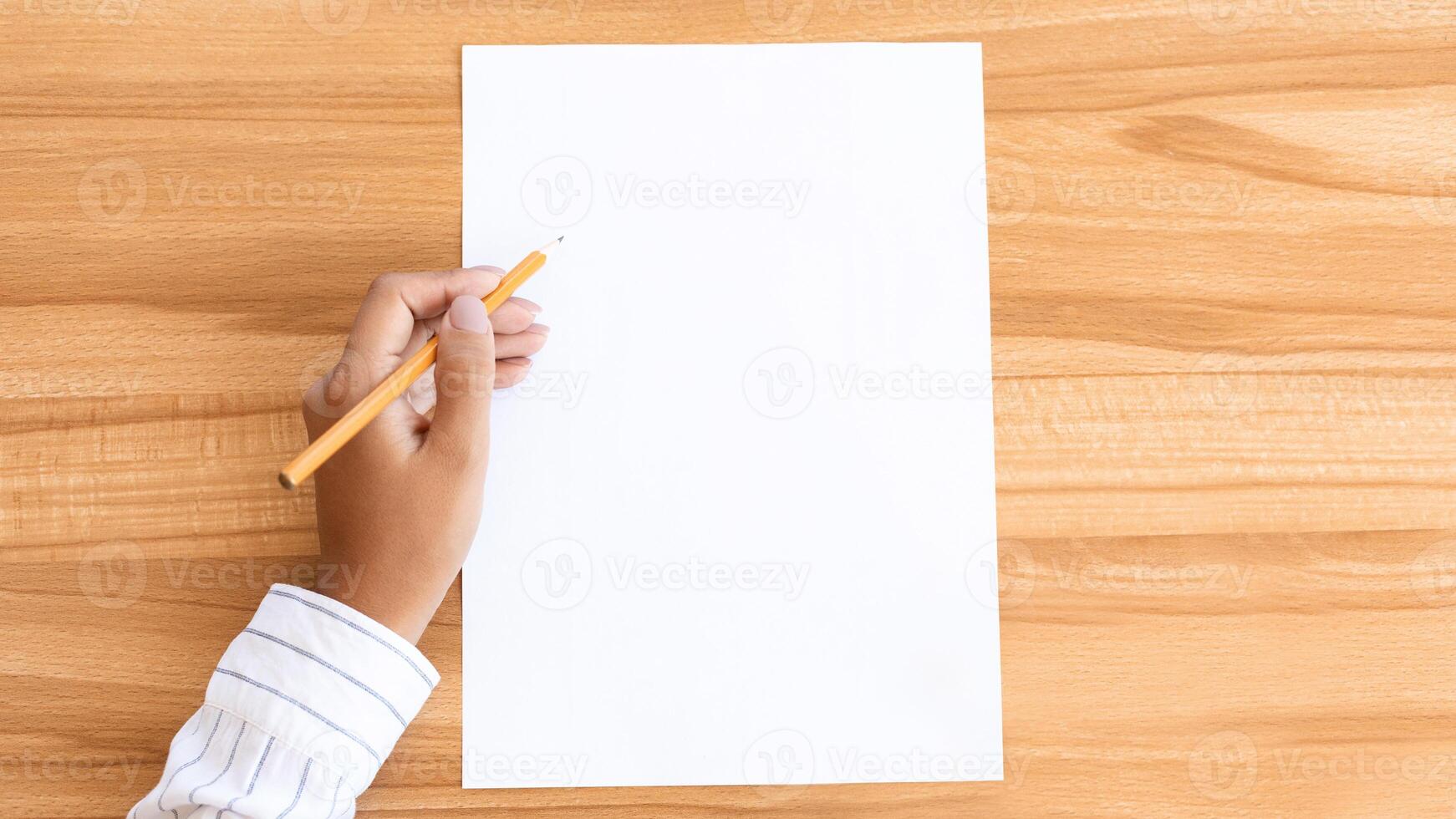 Top view closeup of a lady's hand writing on a piece of paper with a pencil, wooden table background photo