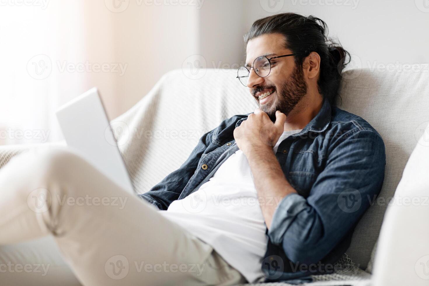 Smiling Eastern Guy With Digital Tablet Relaxing On Couch At Home, Browsing Internet, Checking New App Or Making Online Shopping, Arab Male Enjoying Modern Technologies And Domestic Leisure, Closeup photo