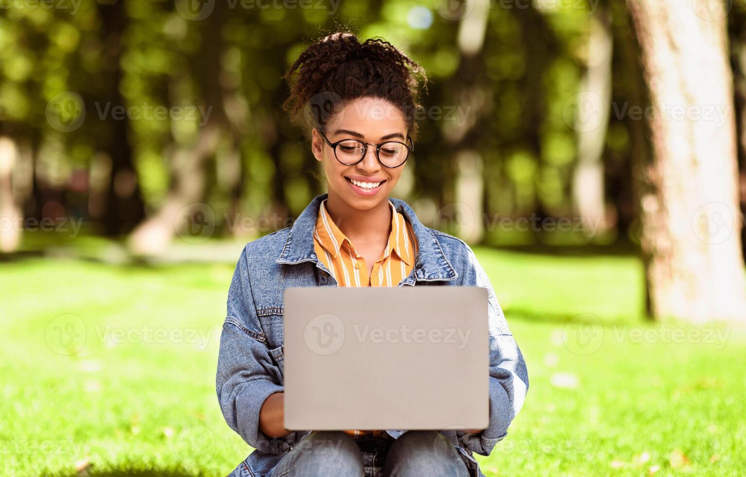 E-Learning. African American Female Student Using Laptop Computer Learning Online Browsing Internet Sitting In Park Outdoors. Distant Education, Educational Website Concept photo