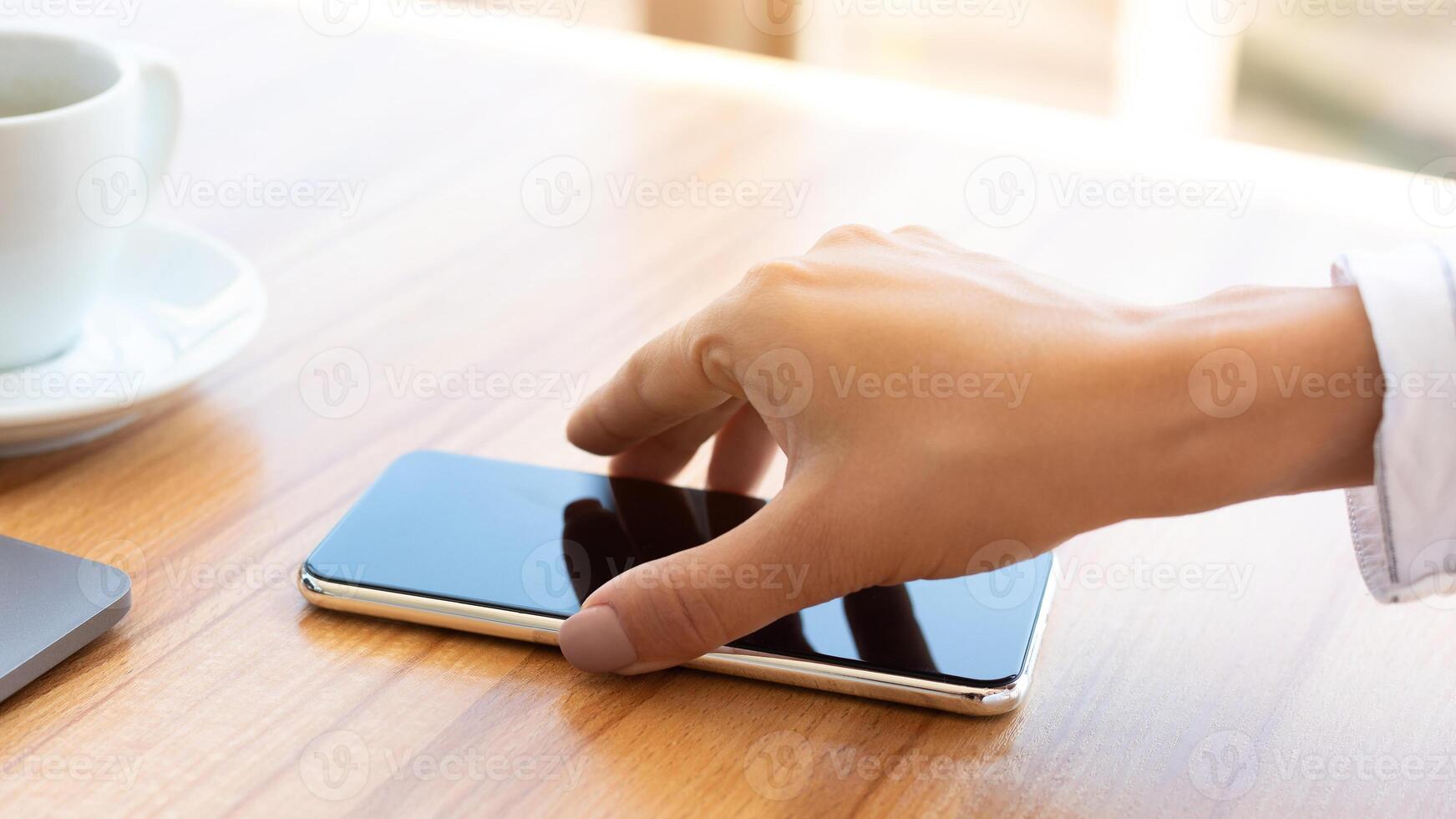 Side view shot of woman's hand holding smart phone, taking or putting it on desk photo
