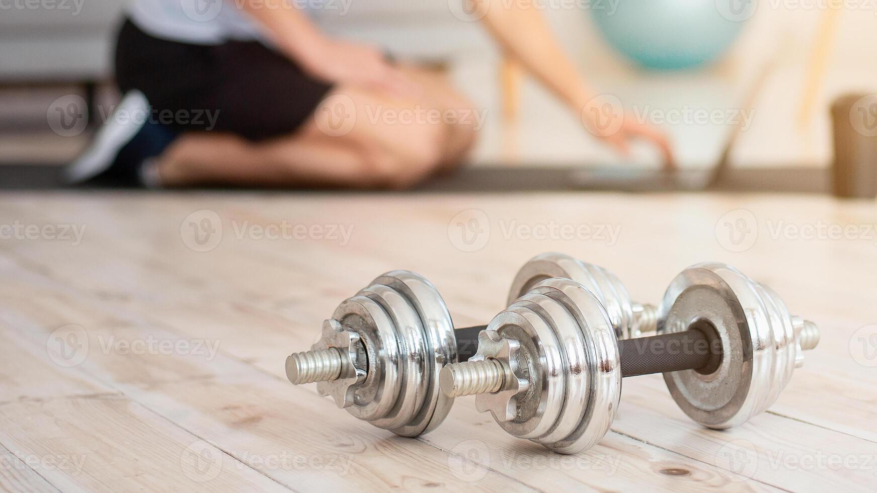 Workout during stay at home COVID-19. Dumbbells close up, young man sitting on mat and working on laptop with sport equipment, free space photo