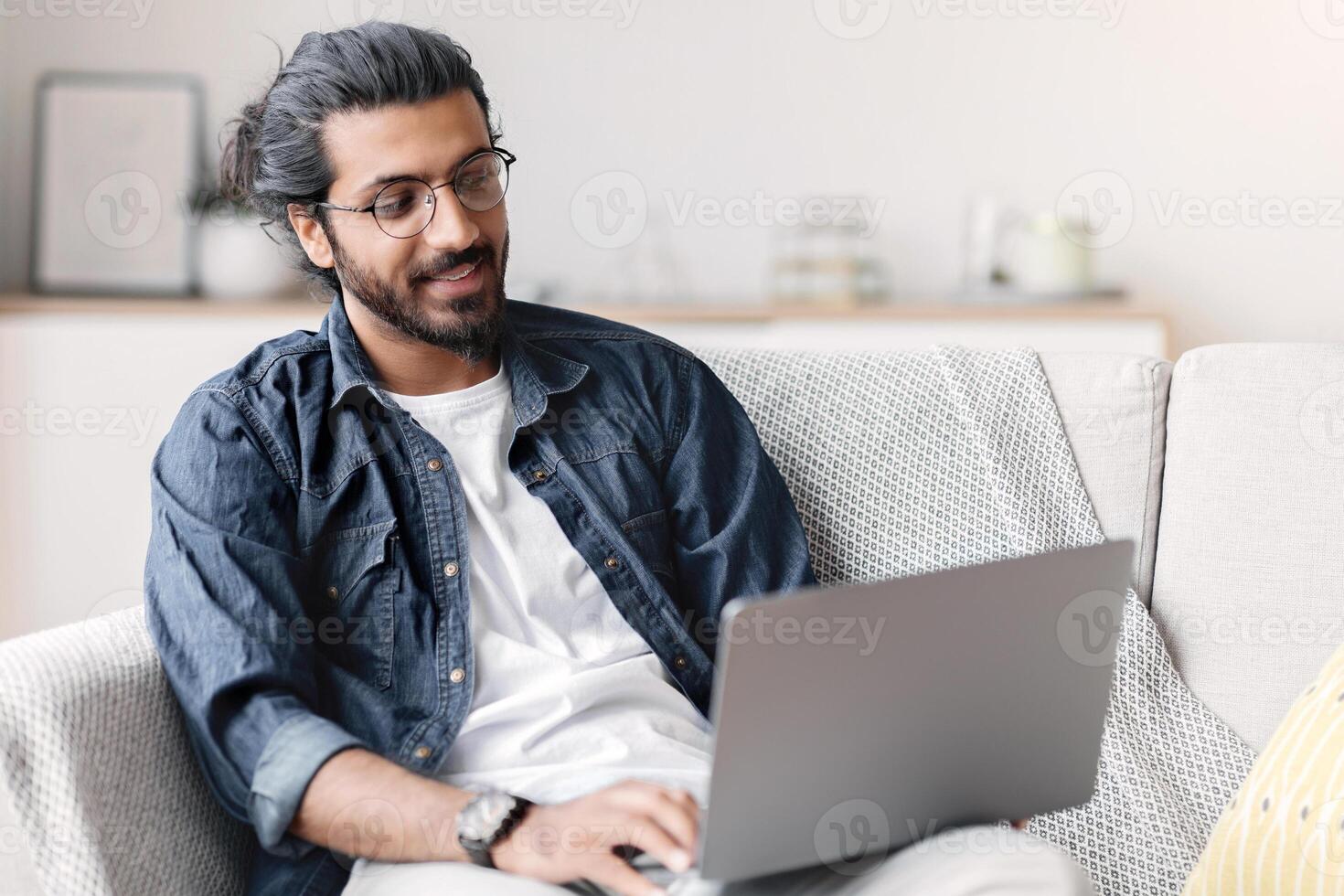 Remote Work. Handsome Eastern Freelancer Guy Working With Laptop At Home, Arab Millennial Man Sitting On Couch In Living Room And Using Computer, Enjoying Distance Job Opportunities, Copy Space photo