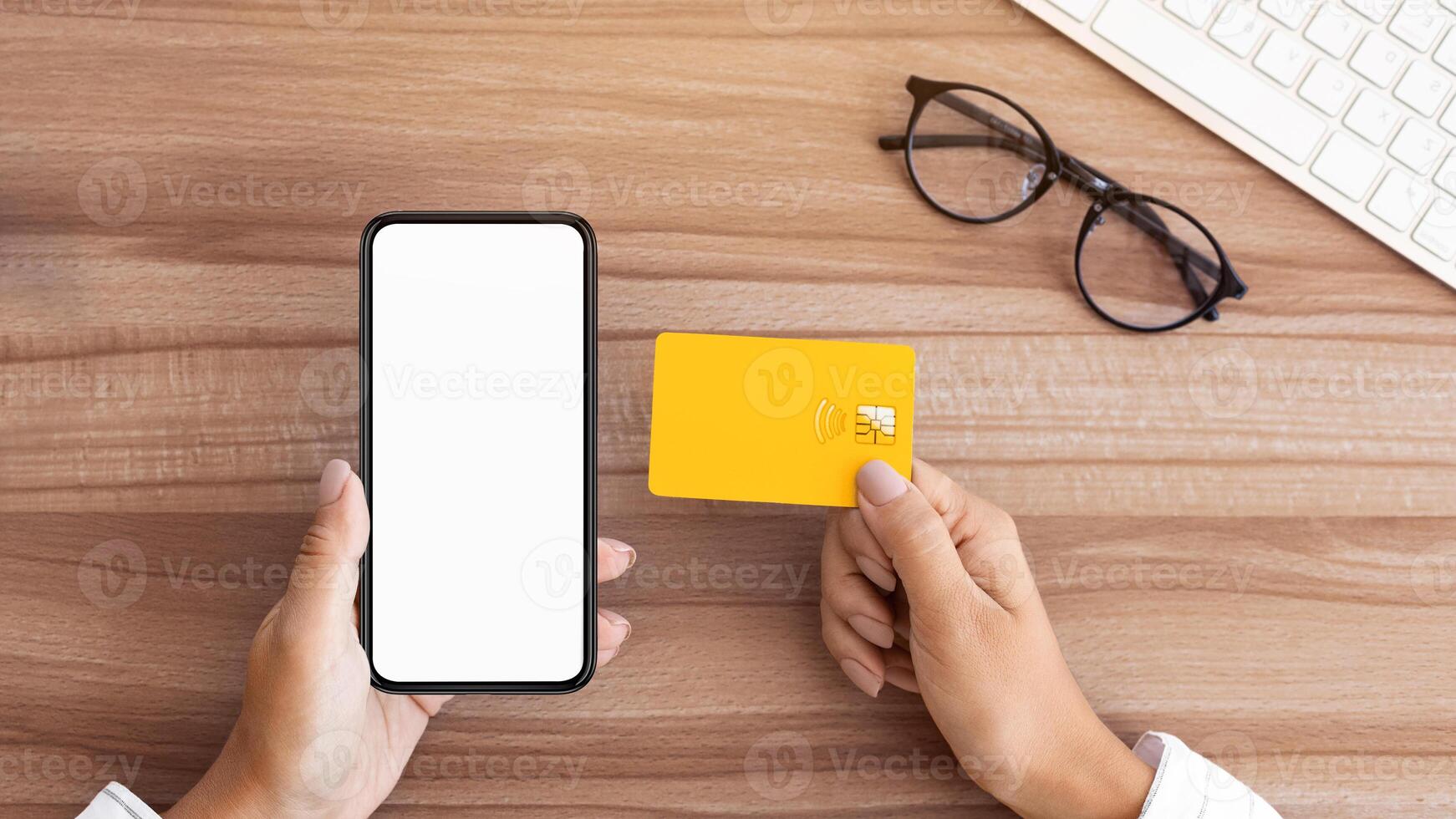 Top view of lady sitting at wood desk, holding credit card and cell phone with white screen, mock up, flatlay, copyspace photo