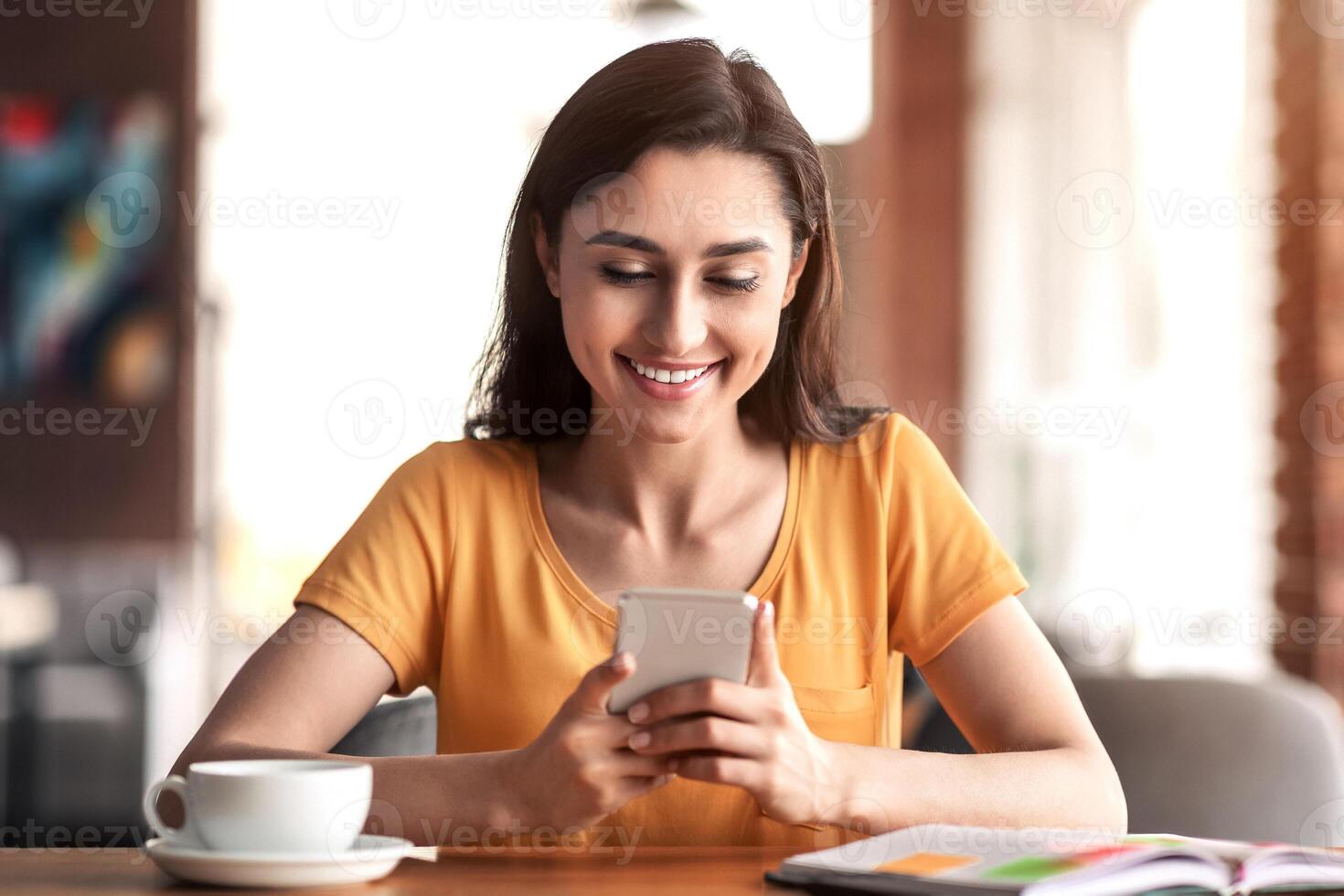 Happy girl sitting at cafe, drinking tea and using smartphone, looking for part-time job, copy space photo