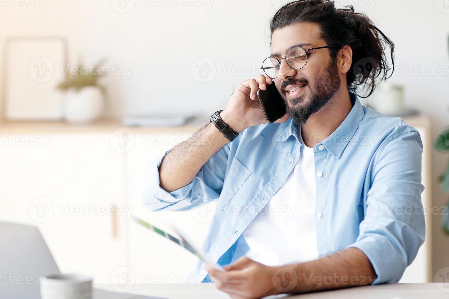 Western Man Freelance Designer Talking On Cellphone With Client, Discussing Future Project, Sitting At Desk In White Home Office With Color Swatches, Choosing Gamma For Interior, Copy Space photo