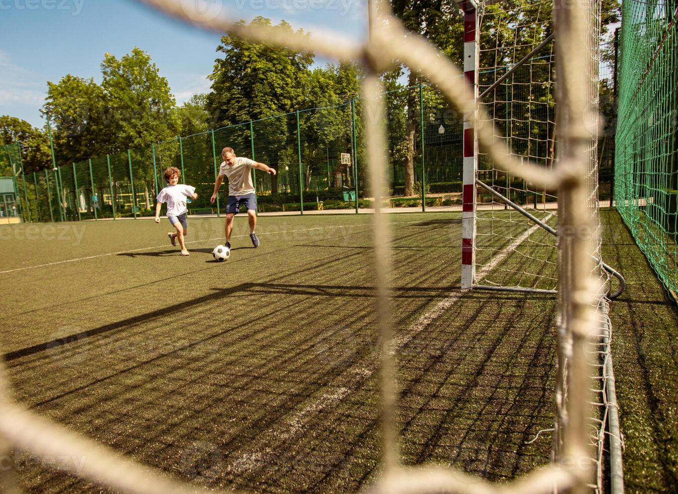 Soccer Match. Two men playing football on the pitch, following the ball, trying to score a goal, view through the net photo