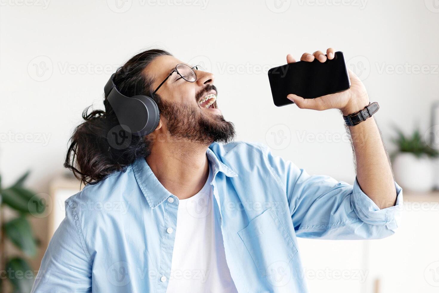 Benefits Of Freelancing. Cheerful Arab Guy Listening Music And Singing While Working At Home Office, Joyful Man Using Cellphone As Microphone, Enjoying Self-Employment And Remote Job, Free Space photo