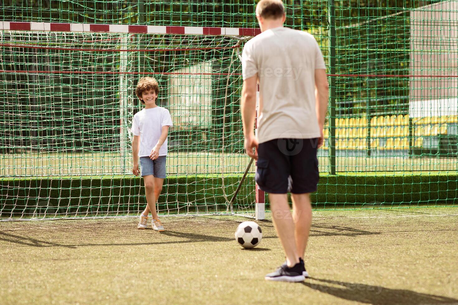 Match. Portrait of two men playing soccer together, little guy standing in the goal waiting for a ball photo