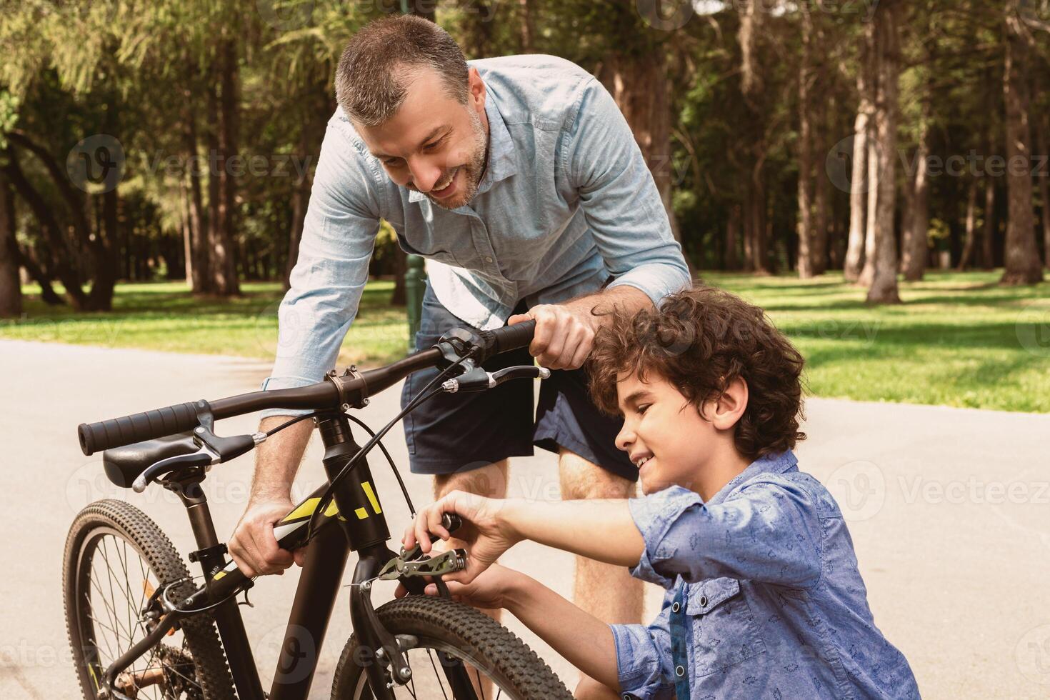 Maintenance. Close up portrait of smiling adult man and boy fixing bike using wire cutter at public park, father holding bicycle, son repairing with clippers, outdoors, selective focus photo