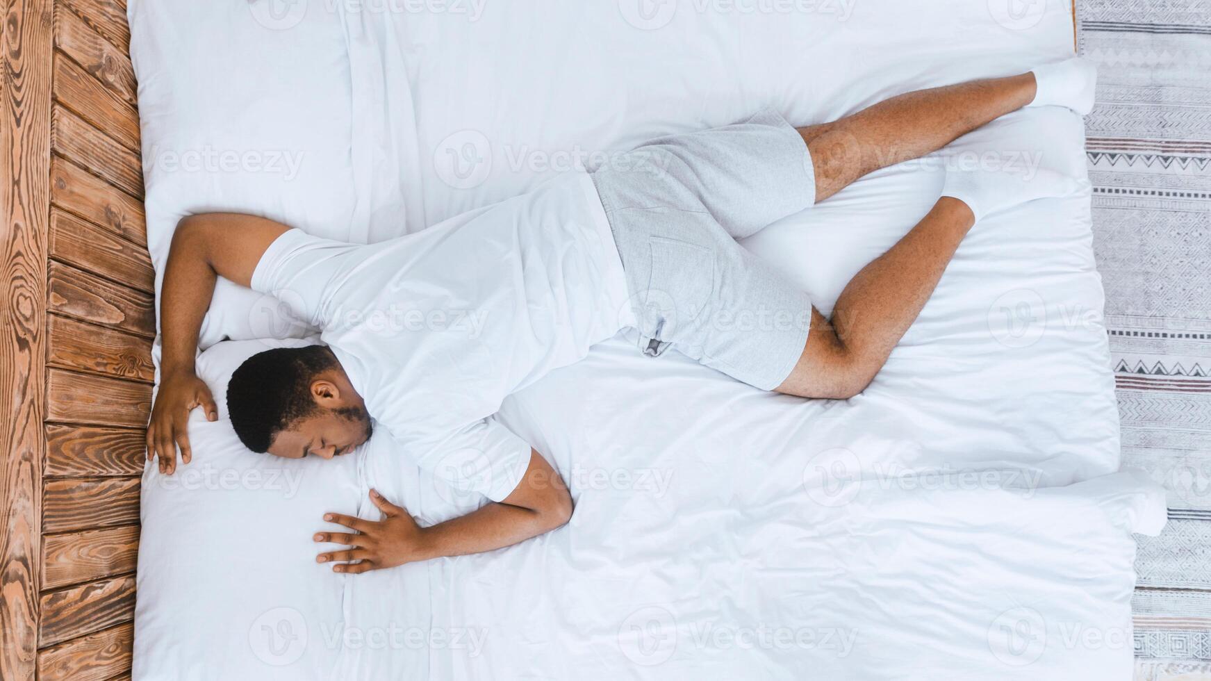 Fast Asleep African Man Sleeping Lying On Stomach Resting Peacefully In His Comfortable Bed In Bedroom At Home. Recreation, Time To Rest And Nap, Deep Male Sleep Concept. Top View, Panorama photo