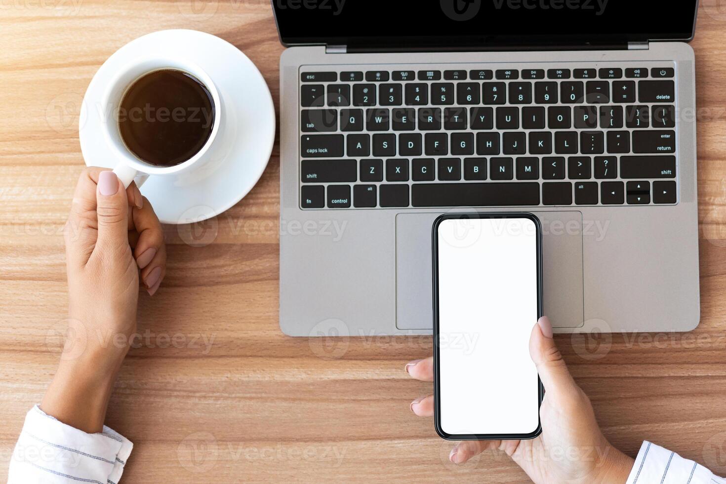 Modern Workplace. Top view of lady holding smart phone with white screen for mock up and cup of coffee photo