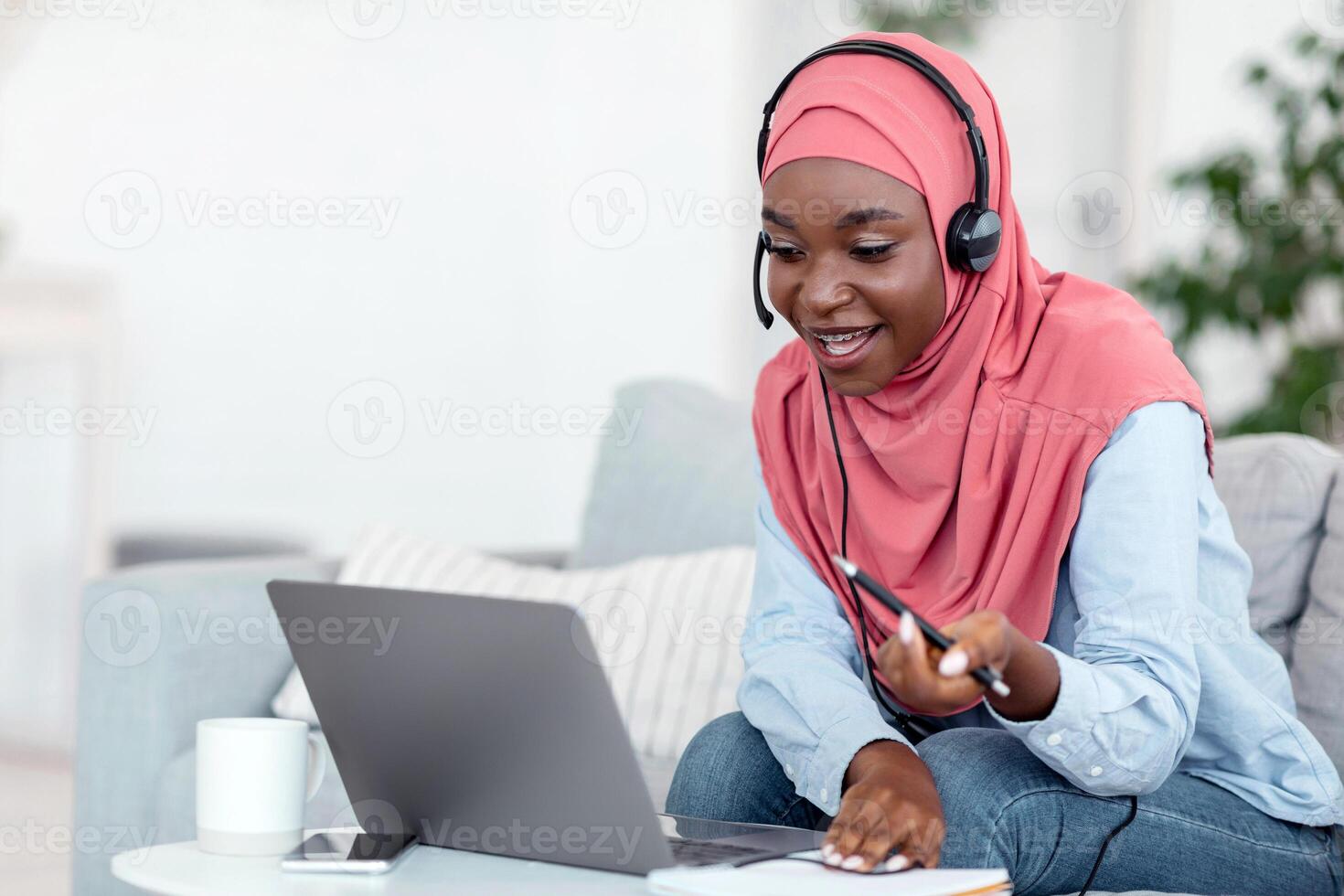 Online Tutoring. Friendly black muslim female tutor having call with students, talking at laptop camera, sitting on couch at home photo