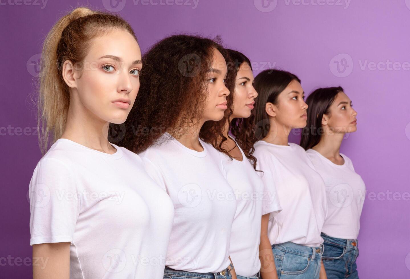 Group Of Serious Multicultural Women Standing In A Row Posing Together Over Purple Background In Studio, Looking At Camera. Female Unity And Diversity Concept. Selective Focus photo