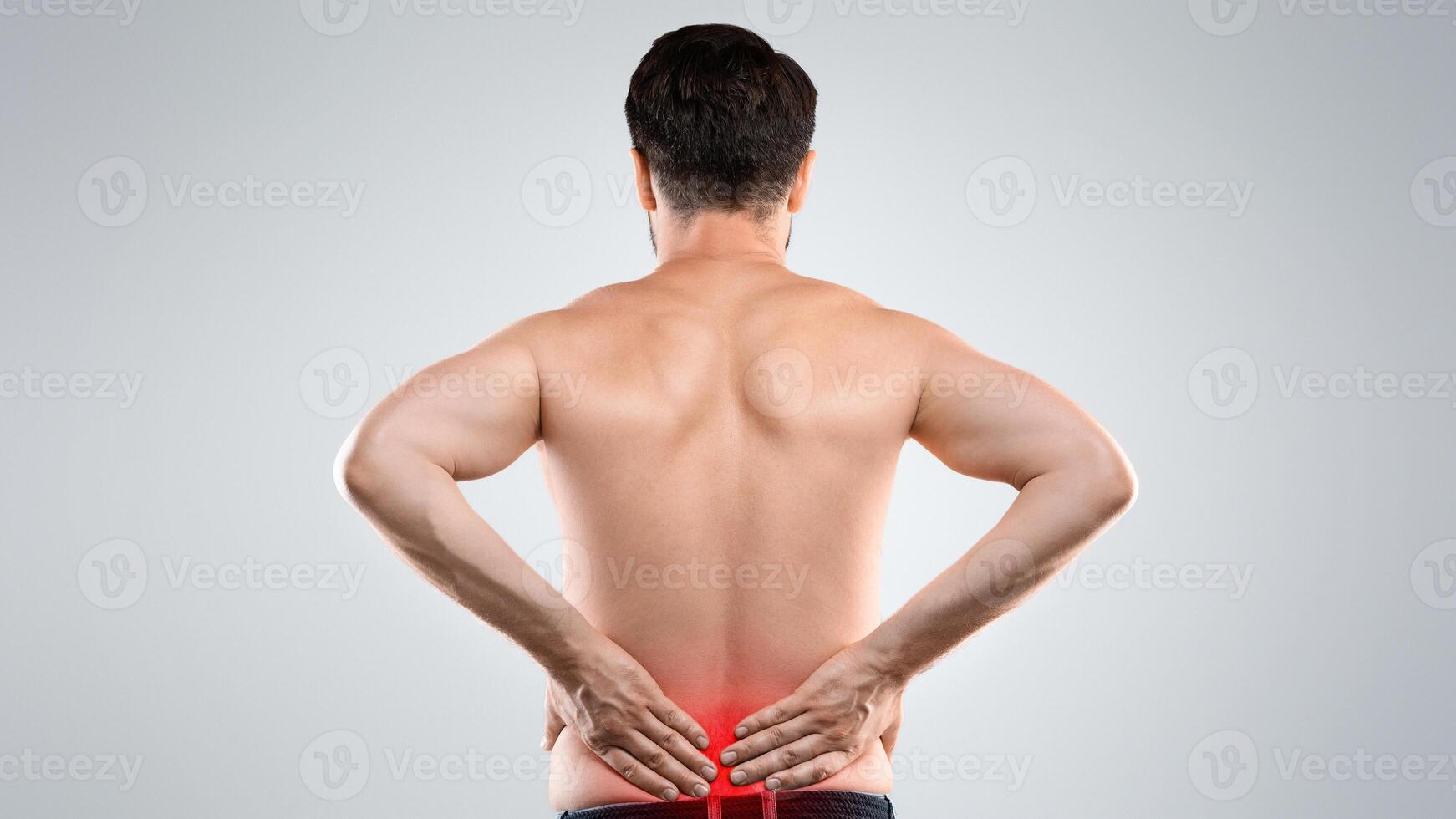Unrecognizable man holding his hands behind his back, pain in spine, inflamed zone highlighted in red, grey studio background, copy space. Rear view of man rubbing lower back, office syndrome concept photo