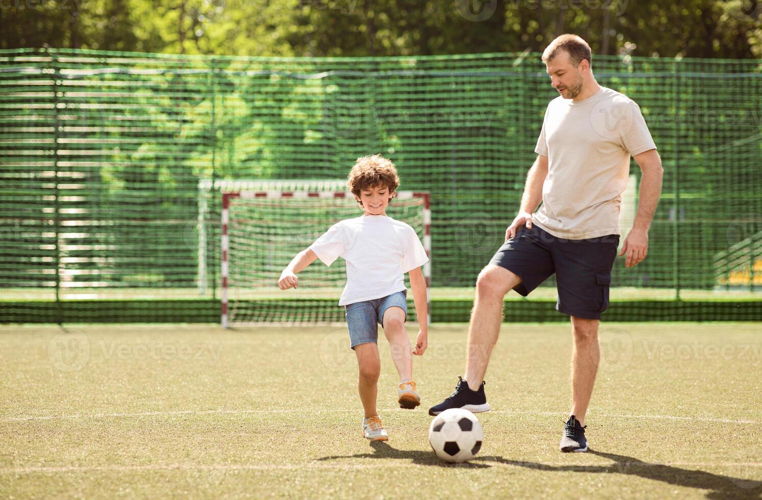 Father and son playing soccer together with ball. Green field in city park at sunny day, copy space photo