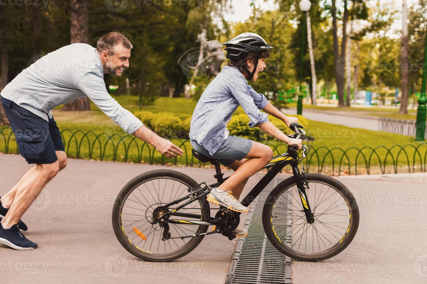Family Time. Dad teaching his son cycling at public park, spending time together on weekend, side view photo