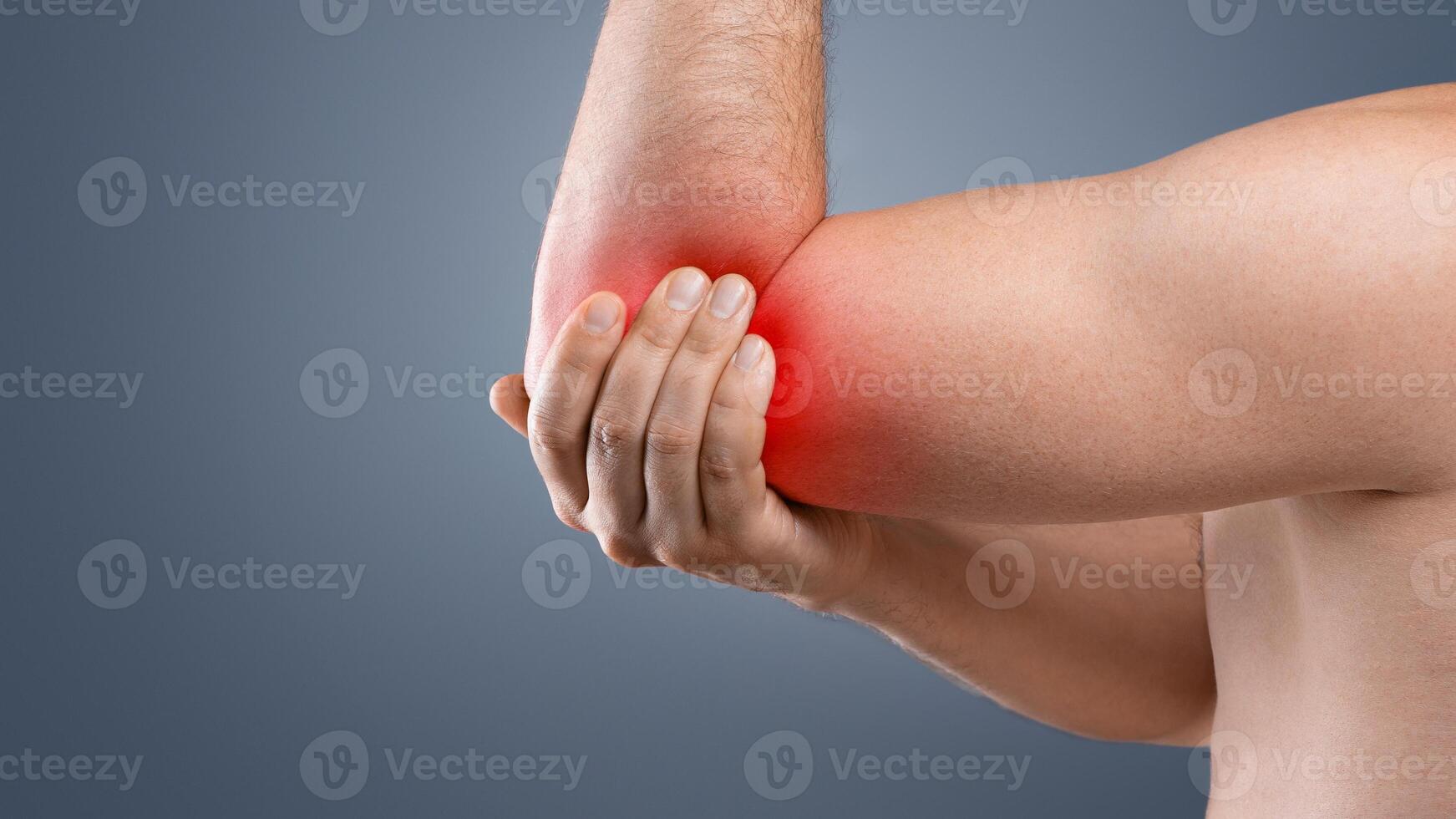 Cropped of topless man having pain in his elbow, touching his injured hand highlighted with red, side view, copy space. Closeup of unrecognizable guy rubbing sore elbow, grey studio background photo