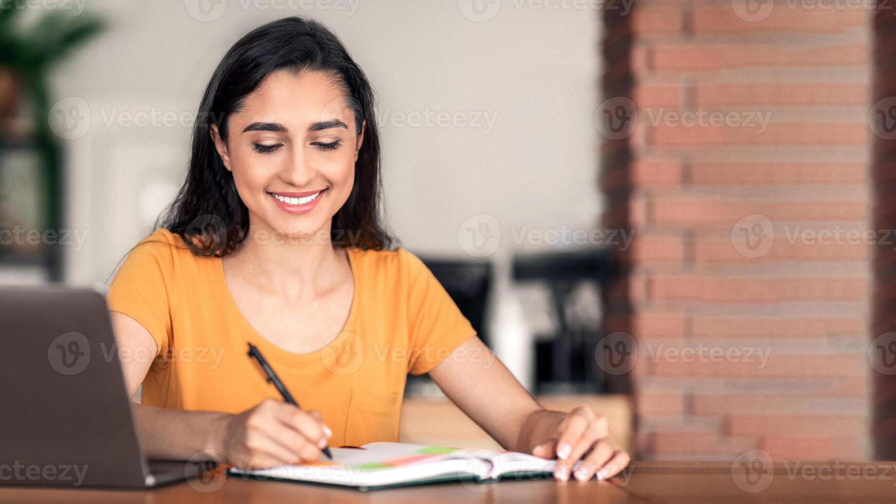Smiling arab girl working online at cafe, making day plan, using laptop photo