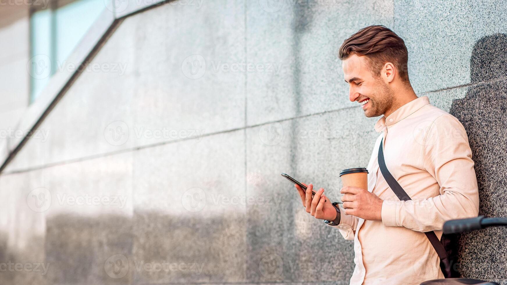 Takes a working break. Happy guy with cup of coffee surfing at smartphone, outdoors, copy space photo