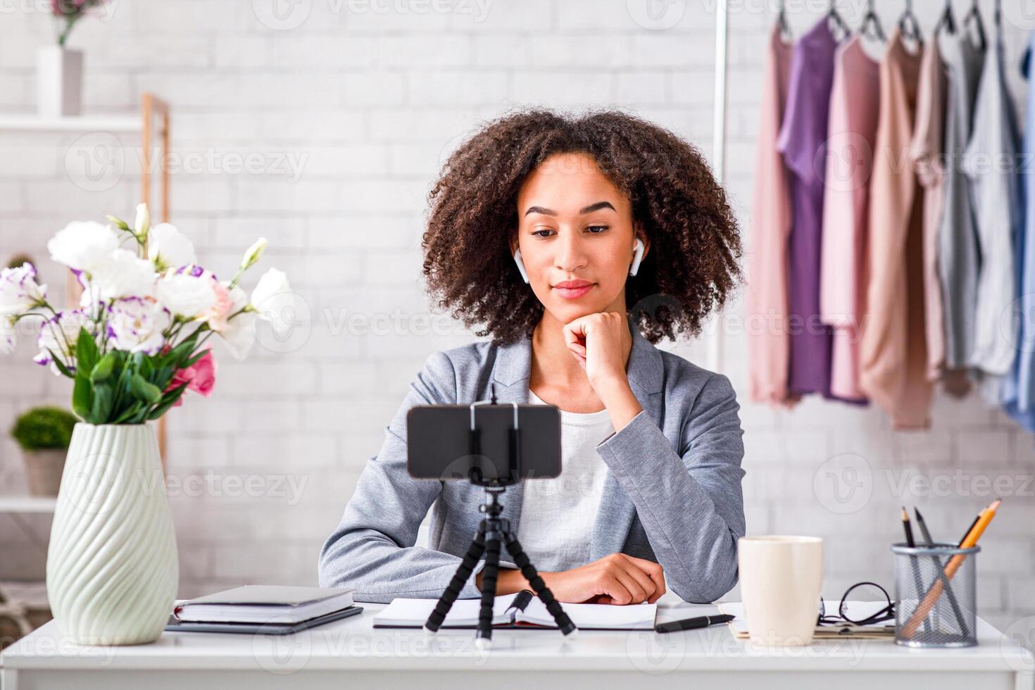 Chatting with followers online during coronavirus outbreak. Serious african american woman with wireless headphones looks at smartphone and makes fashion at home interior, copy space photo