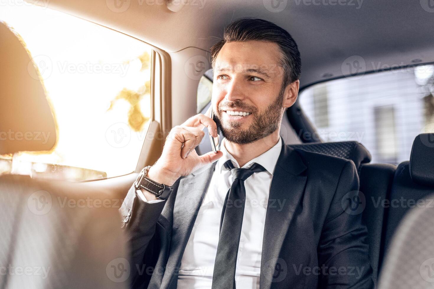 Happy successful businessman talking on phone and using laptop in car photo
