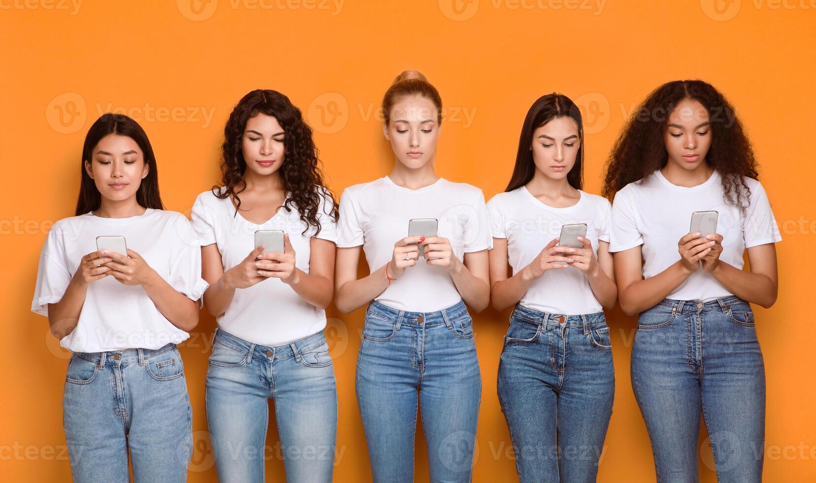 Diverse Girls Using Smartphones Texting In Social Media Apps Standing Over Yellow Background. Modern Communication. Studio Shot photo