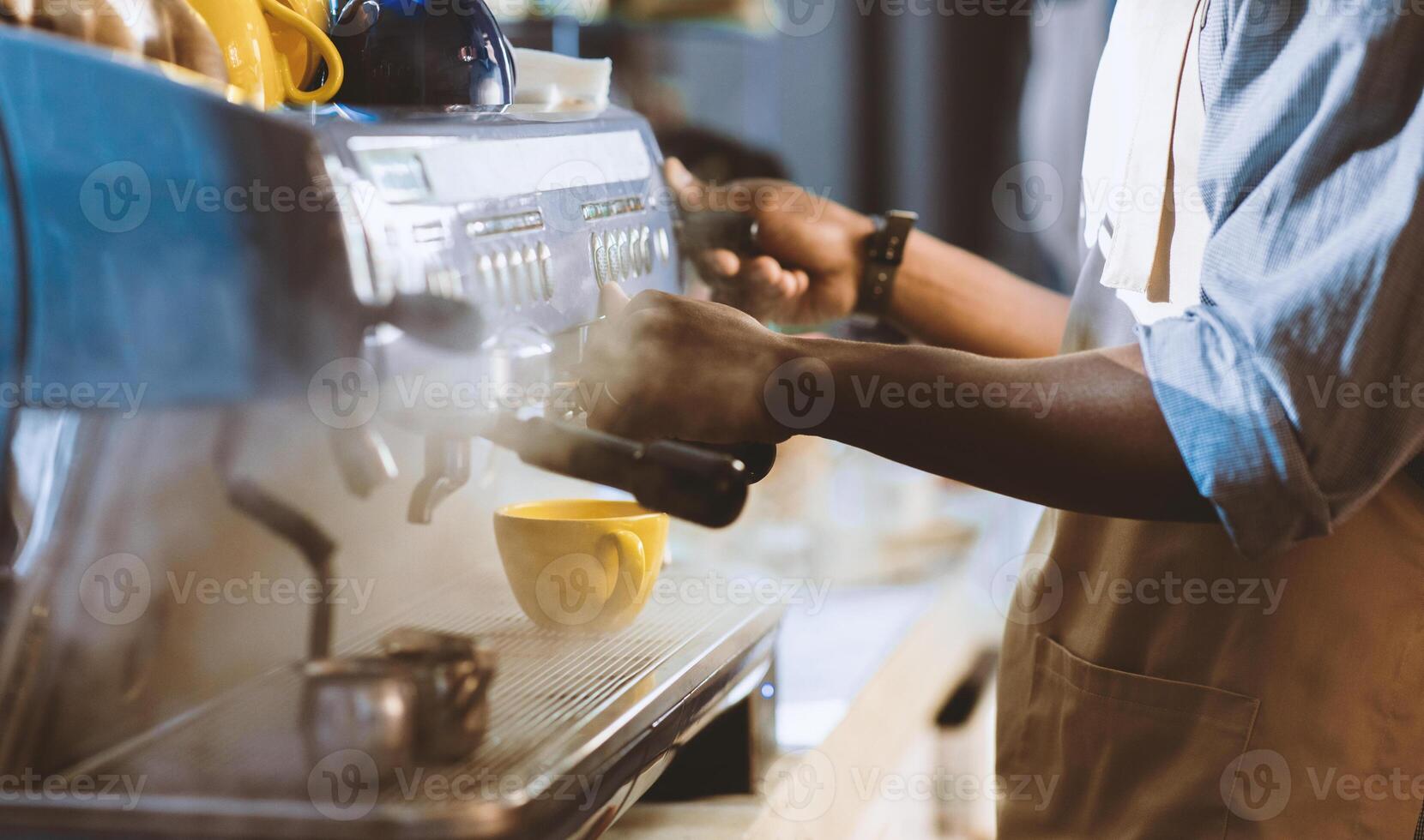 Working with espresso machine in cafe after covid-19. Young african american professional barista guy in apron makes cappuccino on equipment in coffee shop in morning for client, cropped, close up photo