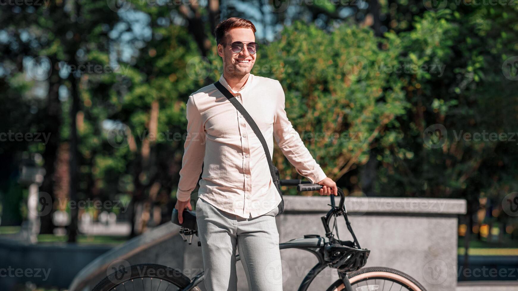 Portrait of smiling handsome hipster businessman in sunglasses with bicycle standing on park background, in autumn photo