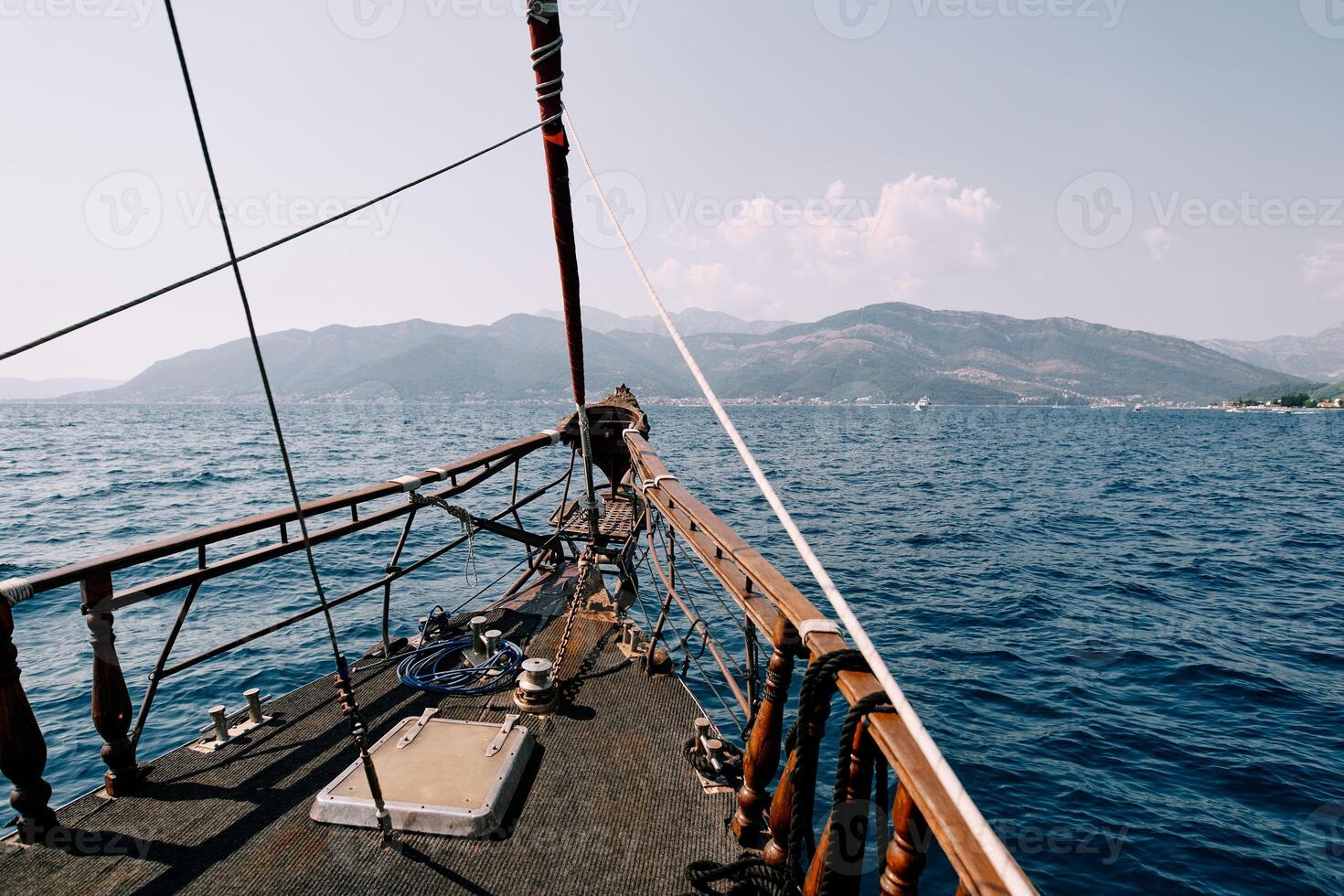 Bow of a wooden sailboat sailing on the sea towards a mountain range photo