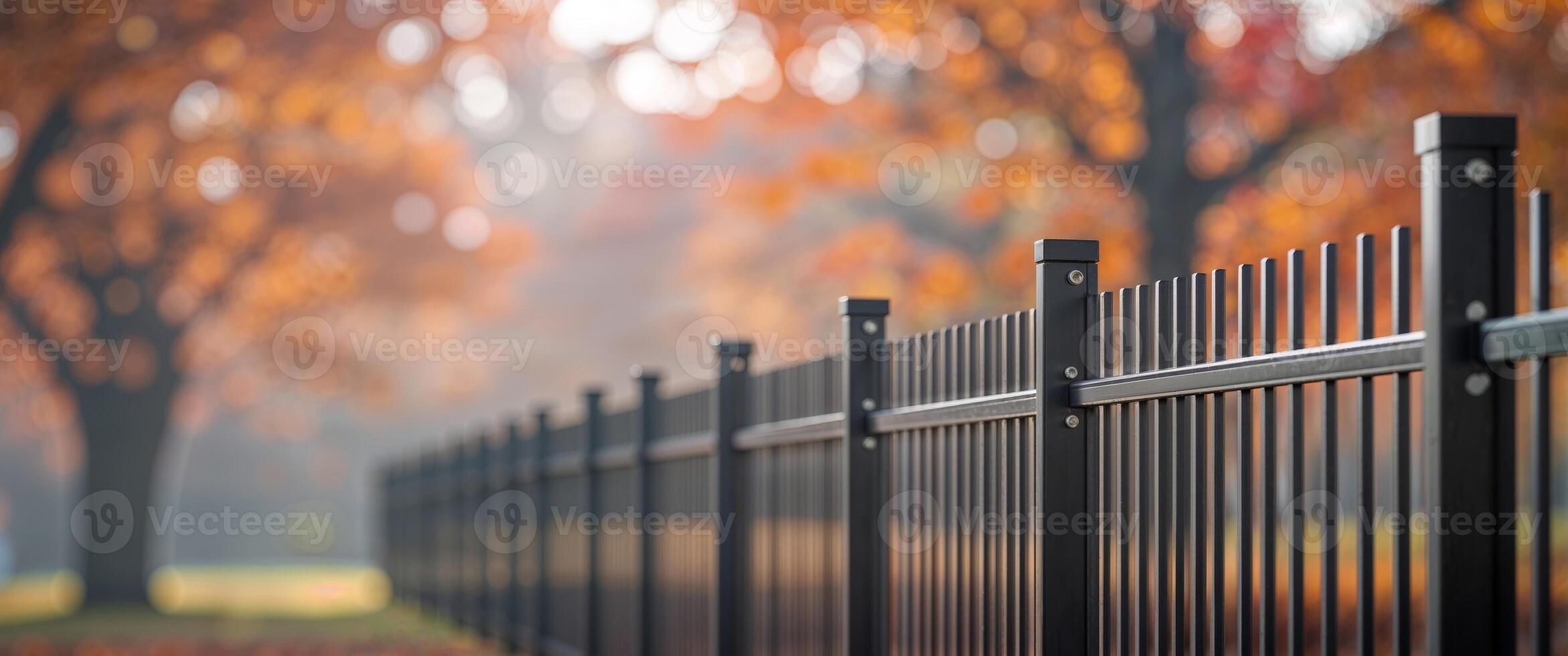 Modern Slatted Black Metal Fence with Blurred Autumn Trees in Soft Focus Outdoor Setting. photo