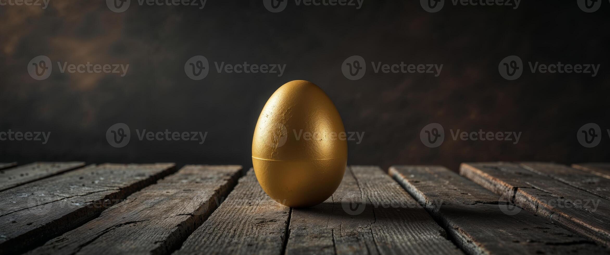 A solitary golden egg rests on a weathered wooden surface. photo