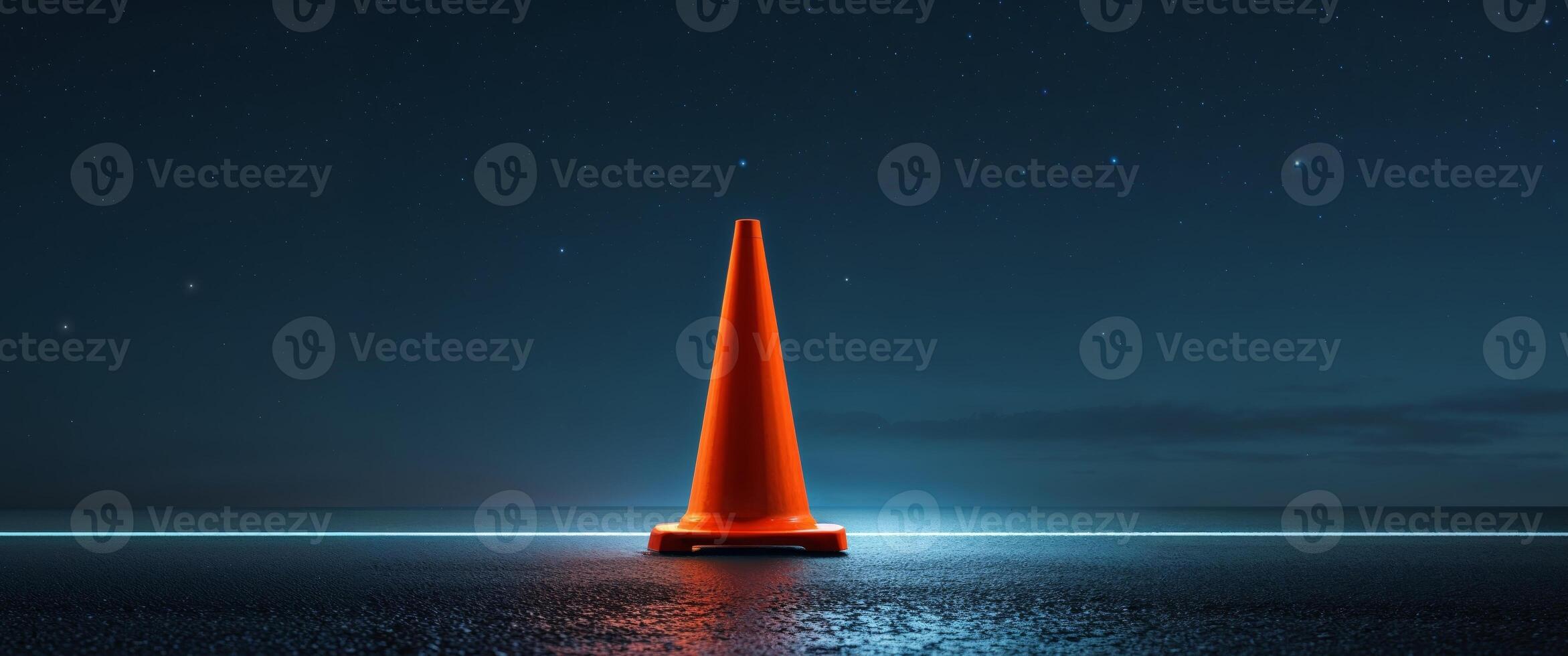 A traffic cone stands on an asphalt road at night photo
