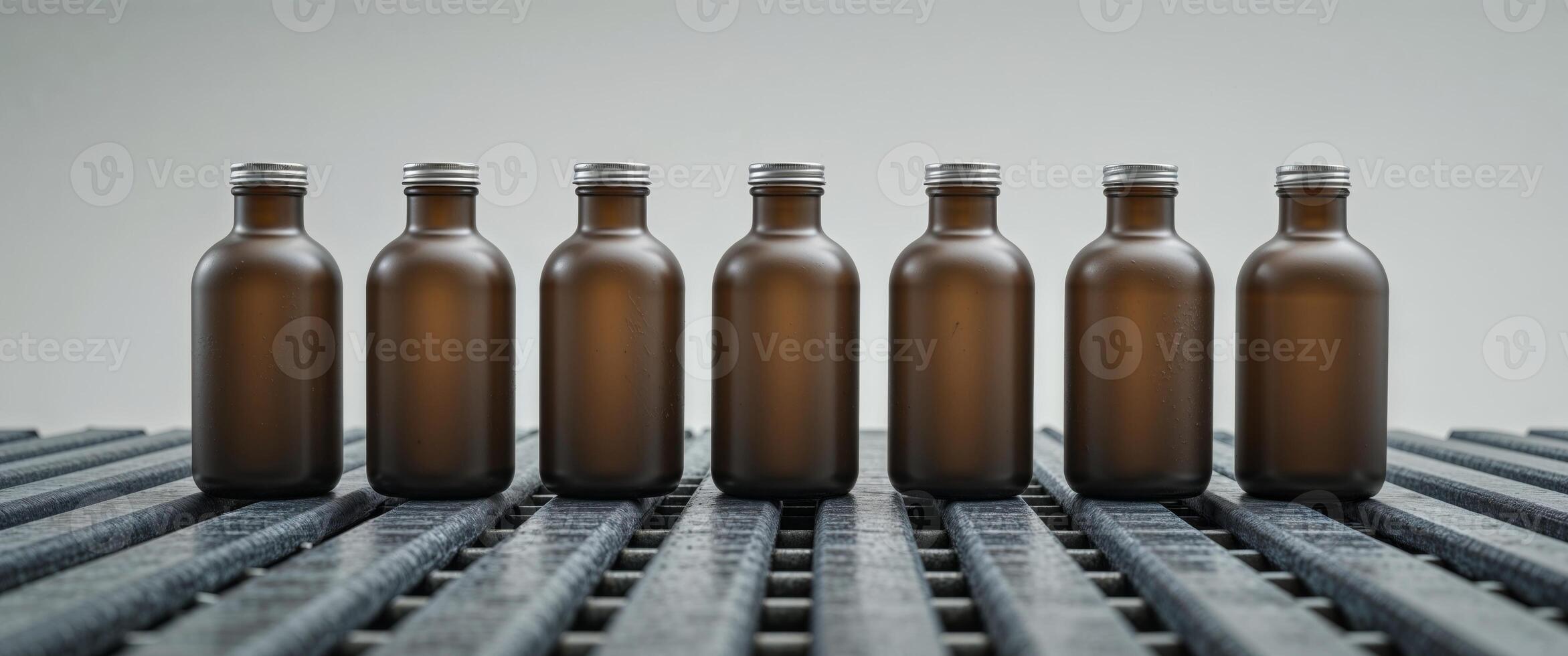 A row of brown bottles with silver lids on a conveyor belt photo