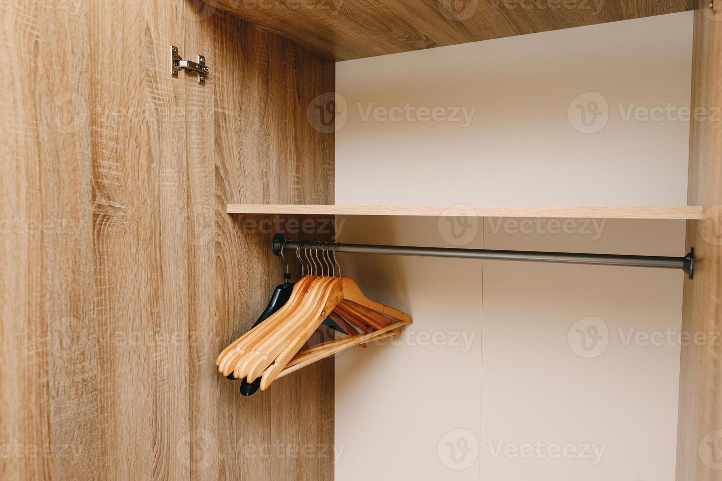 An empty wooden wardrobe featuring hangers and a shelf inside photo