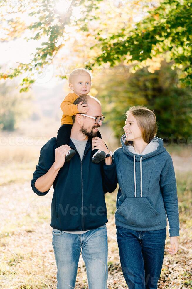 Mom and dad with a little son on his shoulders walk in the park and look at each other photo