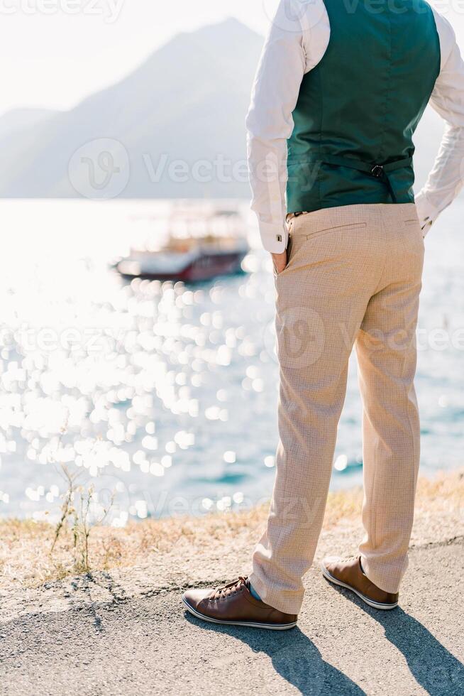 Man with his hands in his pants pockets stands over the sea. Back view. Cropped photo
