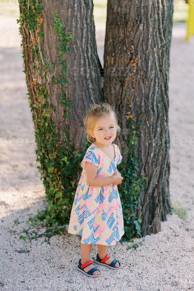 Little smiling girl stands near a tree covered with ivy photo