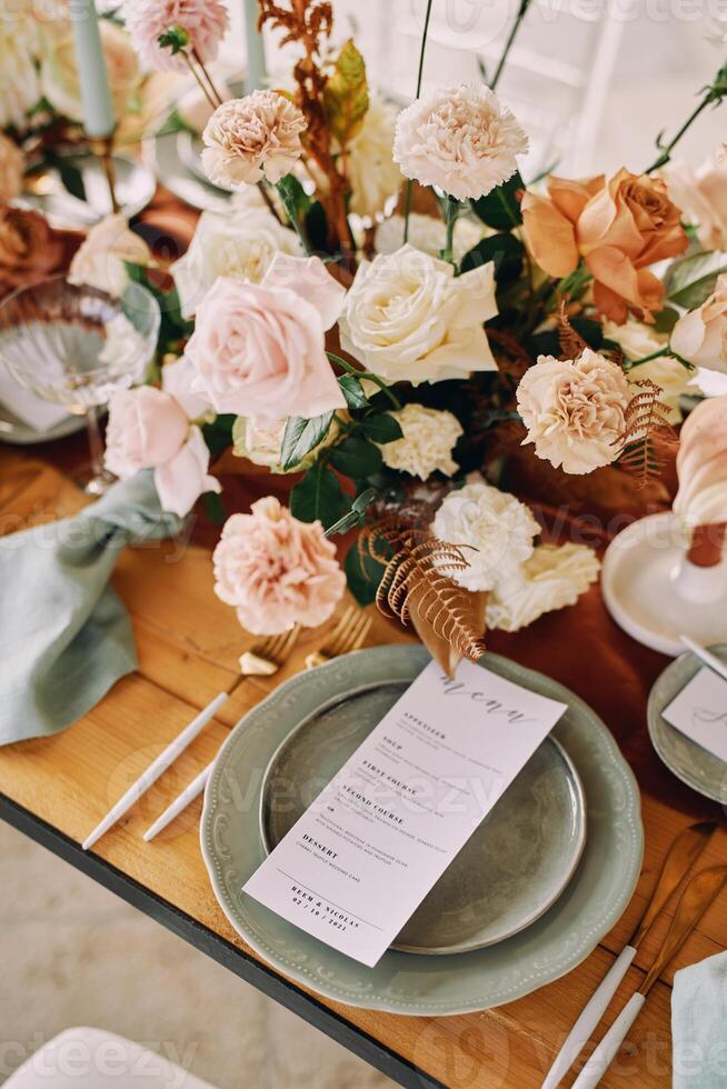 Bouquet of flowers stands on the festive table next to a plate with a menu photo