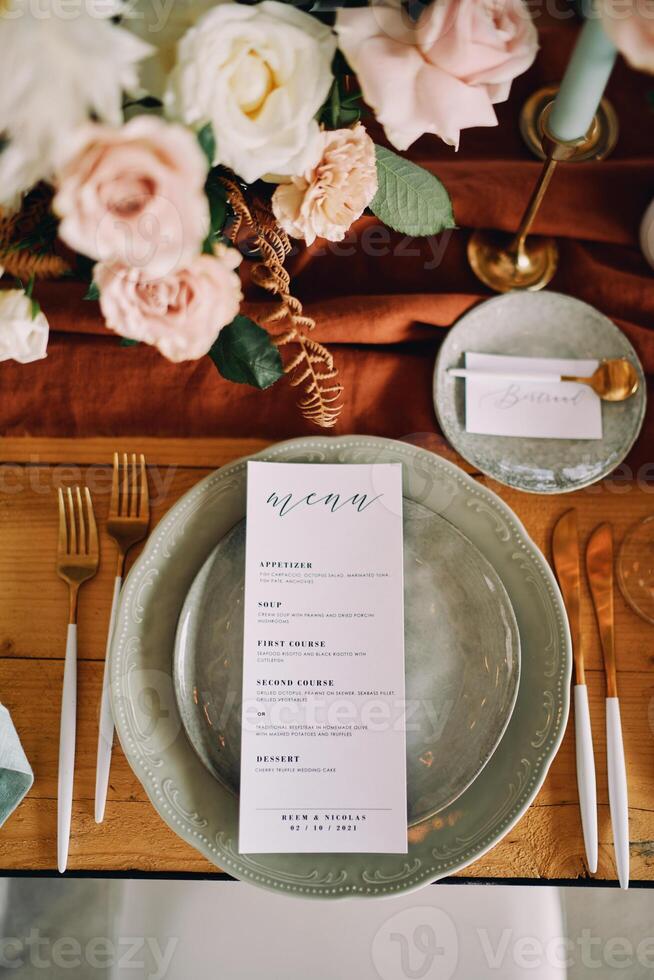 Sheet with a festive menu lies on a plate next to a bouquet of flowers on the table photo