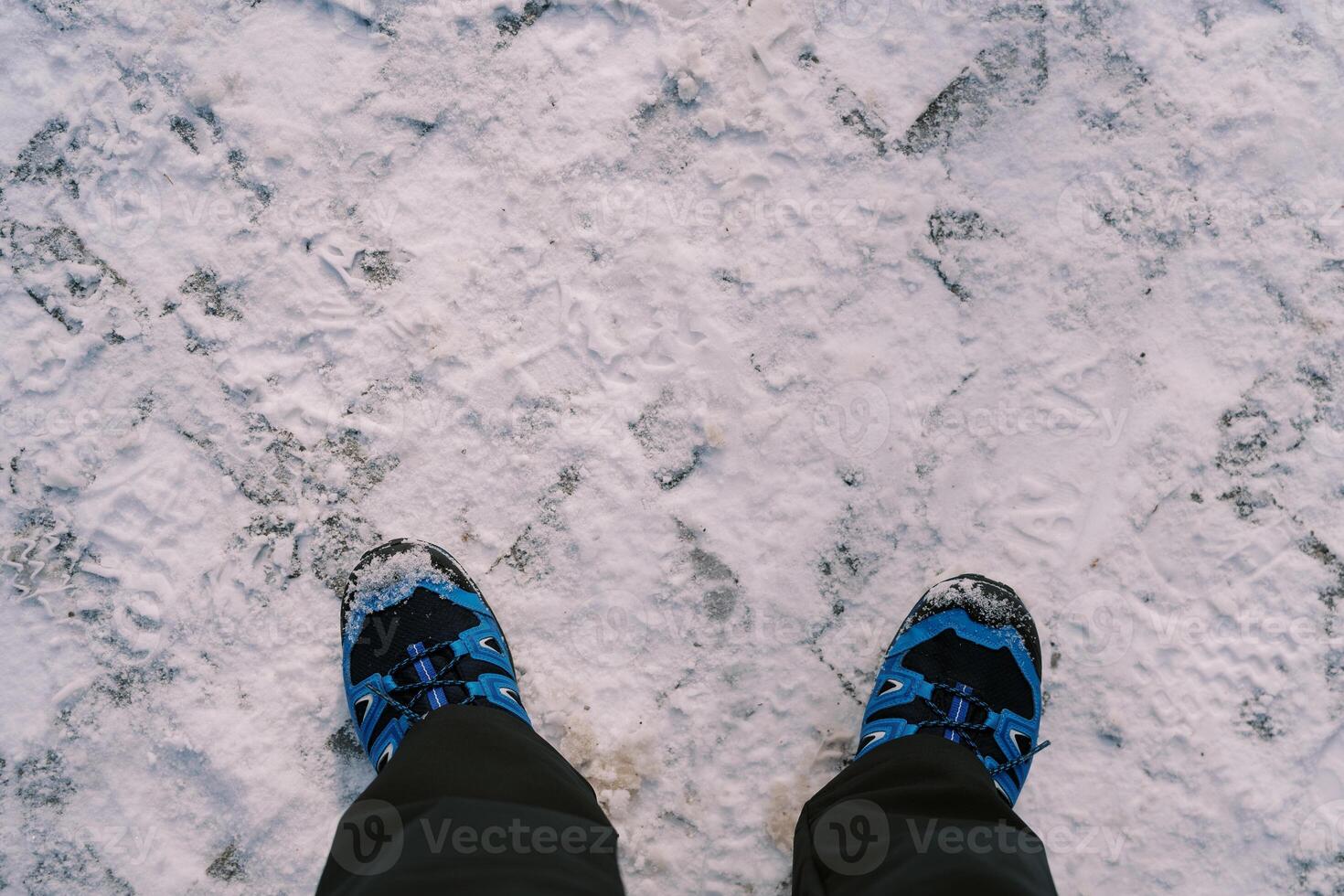 Women legs in boots and ski pants stand on snow-covered paving stones. Top view. Cropped. Faceless photo