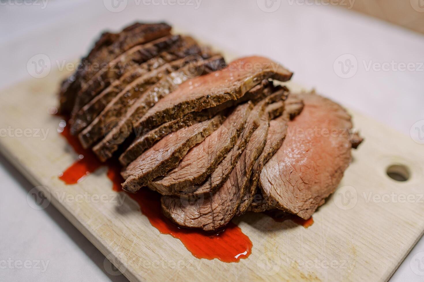 Thin slices of roast beef with blood lie on a wooden cutting board on the table photo