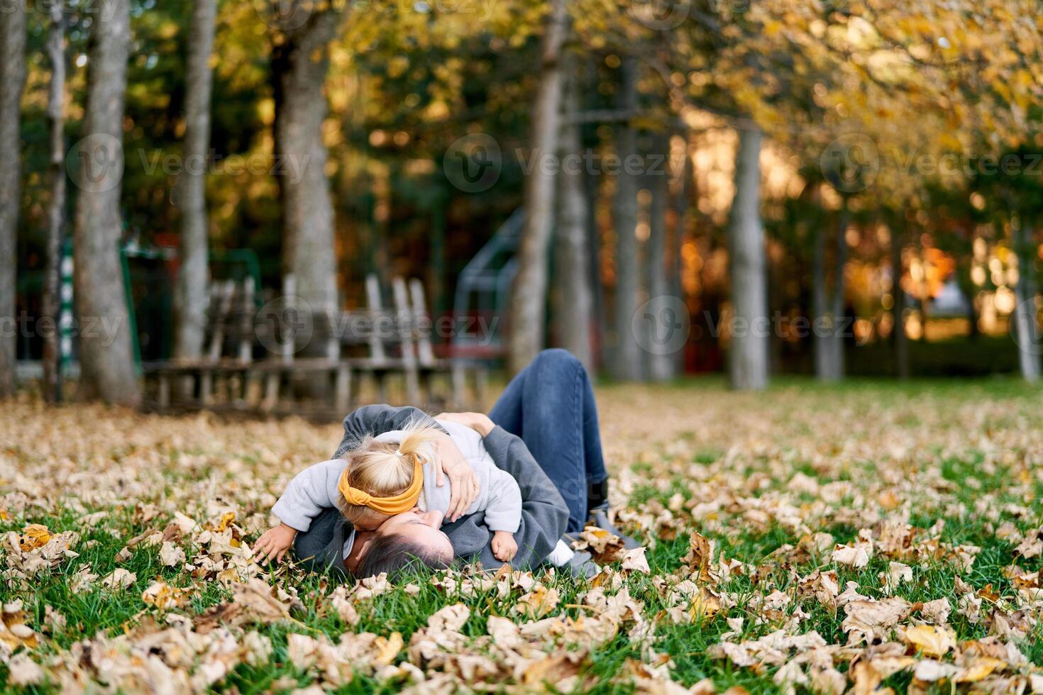 Little girl lies on her mother stomach on the autumn lawn, hugging her photo