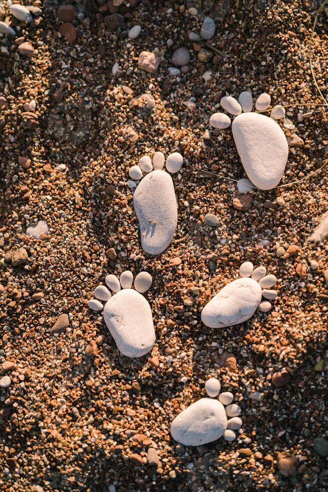 Chain of footprints of bare feet made of pebbles in the sand photo