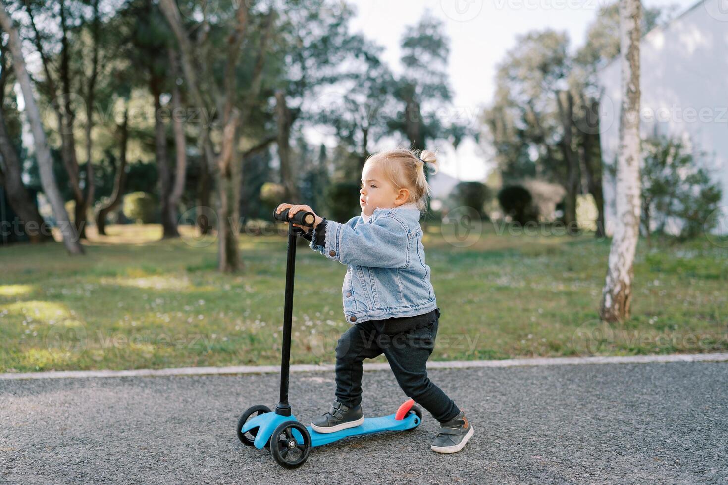 Little girl rides a scooter across an asphalt yard pushing off with her foot photo