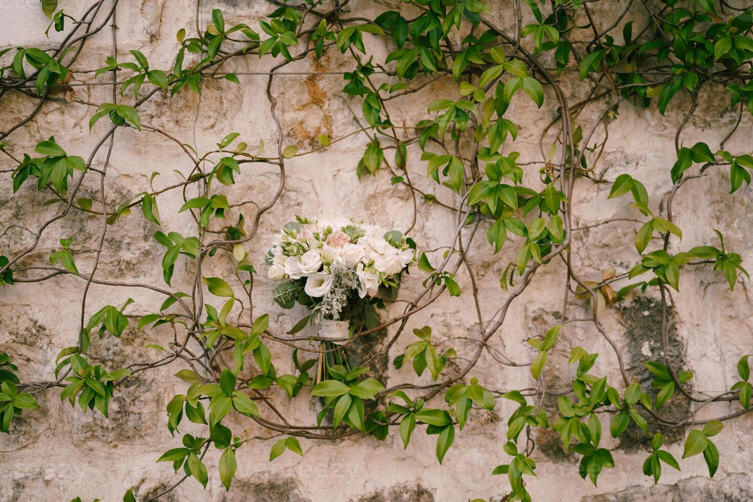 Bride bouquet on the stone wall of an old house entwined with green ivy photo