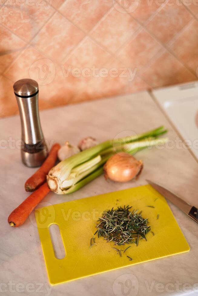 Finely chopped fresh rosemary on a cutting board lies in the kitchen on the table next to vegetables photo
